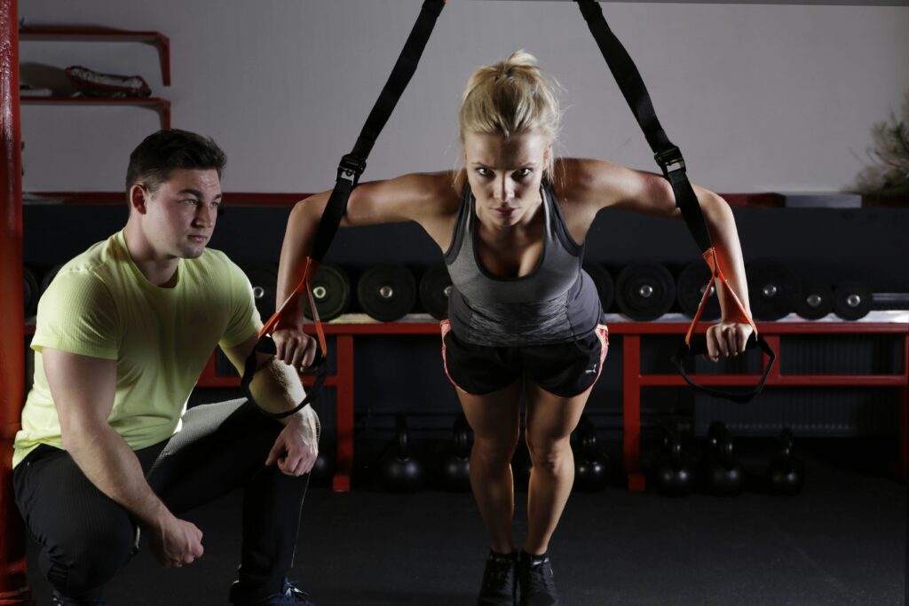 pexels-photo-414029-414029-1 A woman performing strength training with a trainer in a gym setting, showcasing fitness and dedication.